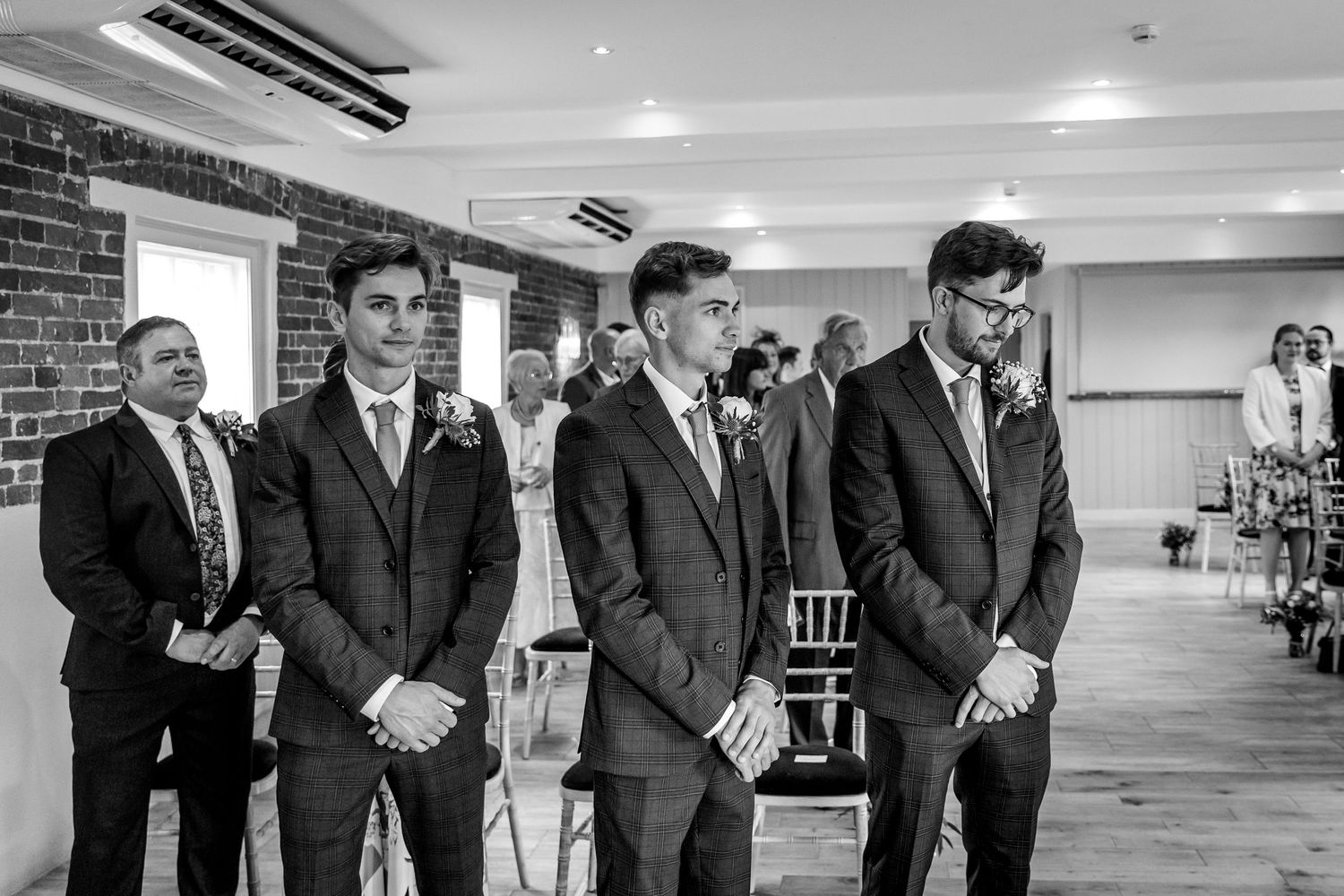 Groomsmen in dark suits standing in line at a modern indoor venue.