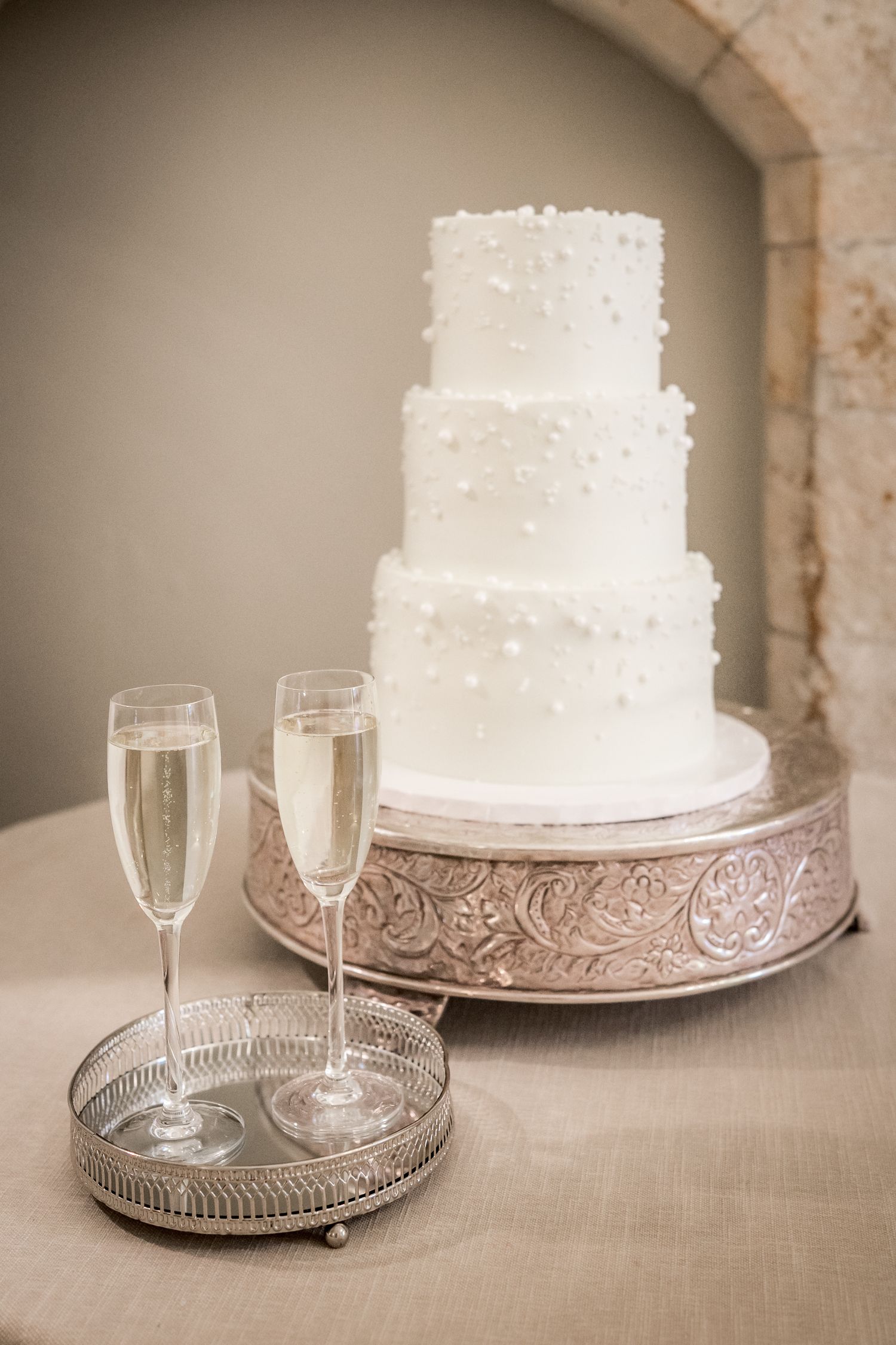 White tiered wedding cake displayed on silver platter with champagne flutes.