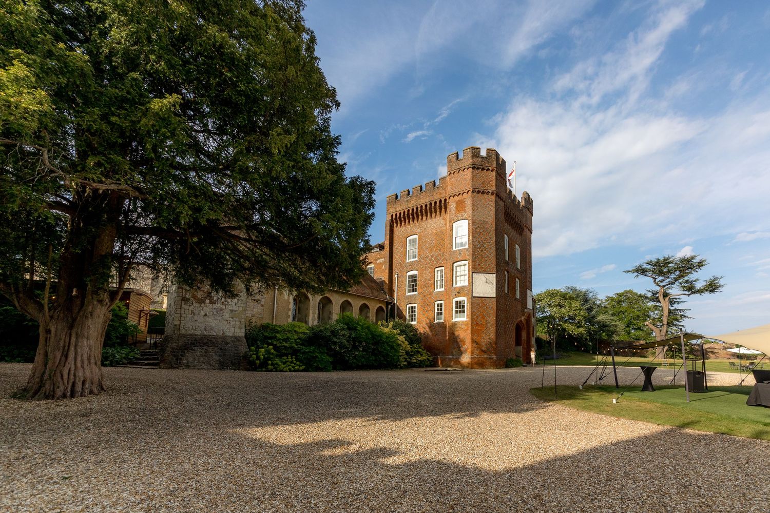 Historic brick castle building with tower set against blue sky and green grounds.