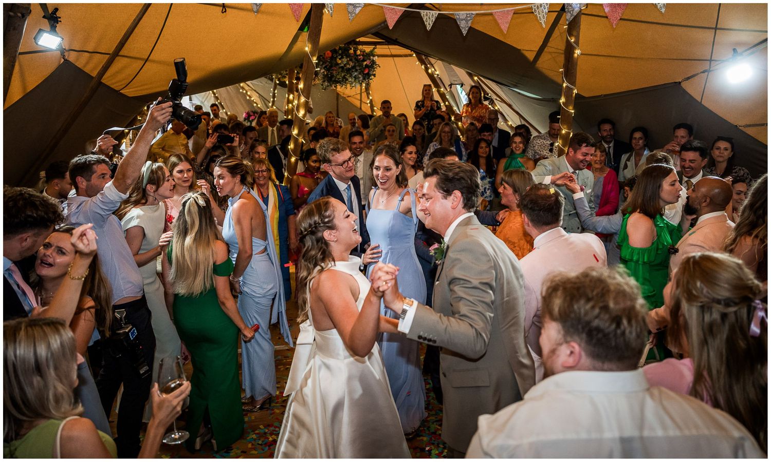 Bride and groom share first dance surrounded by cheering guests inside a decorated tipi at Hampshire's Holywell Estate wedding venue.