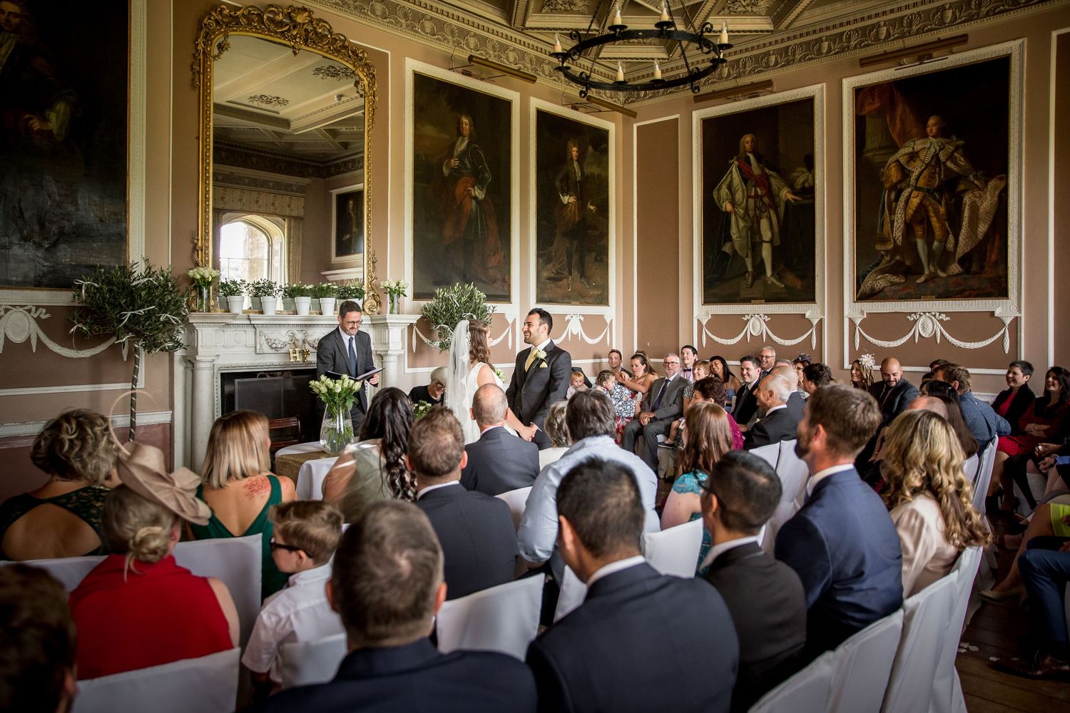 Wedding guests gathered in an ornate room watching a ceremony.