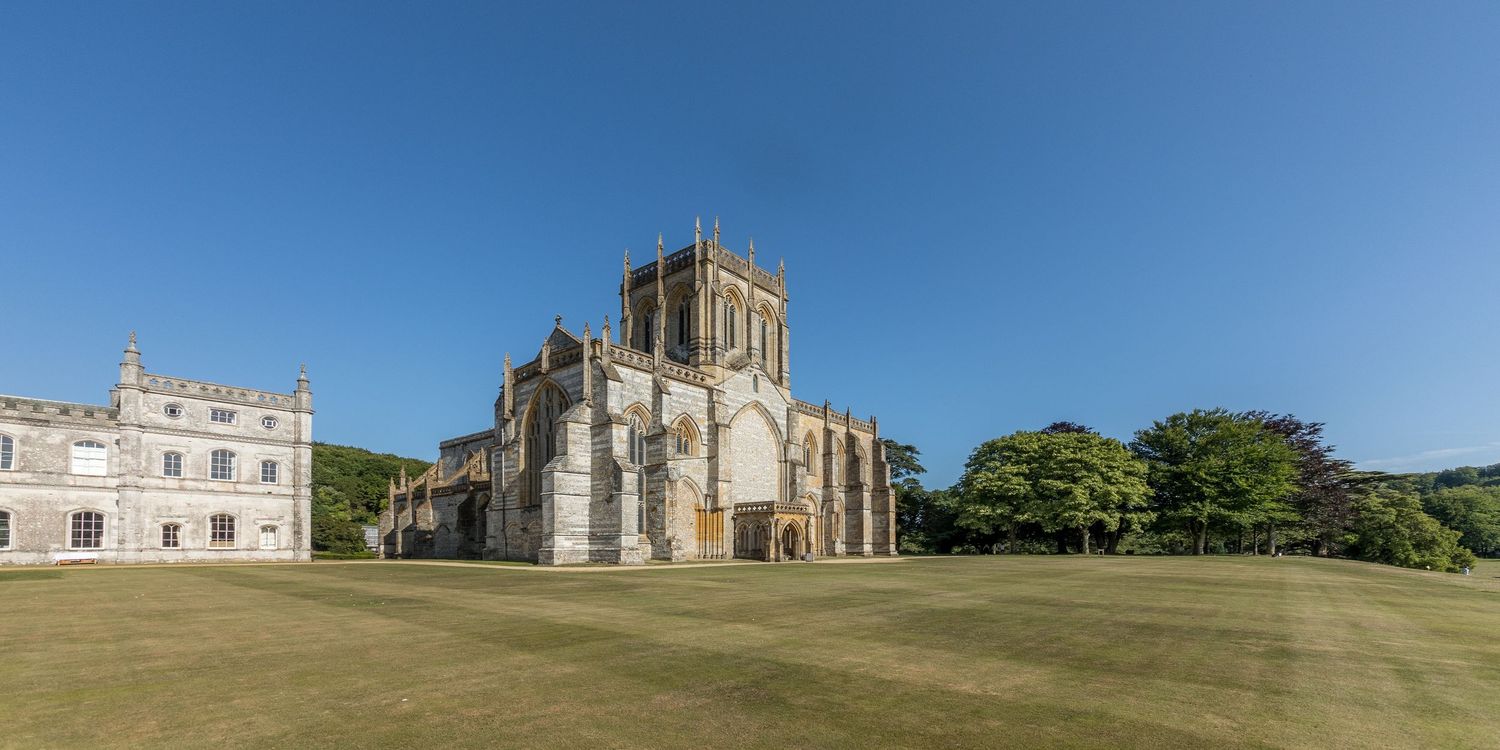 Panoramic view of historic church and manor buildings against clear blue sky.