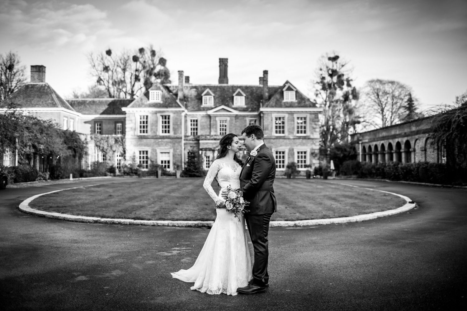 A romantic black and white wedding photo in front of a grand Georgian mansion with a circular driveway.
