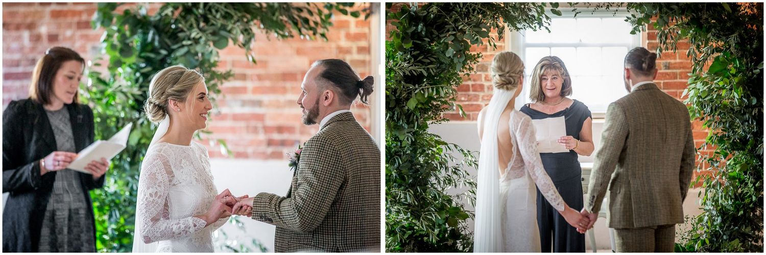 Natural greenery arch frames the wedding ceremony space against rustic brick walls.
