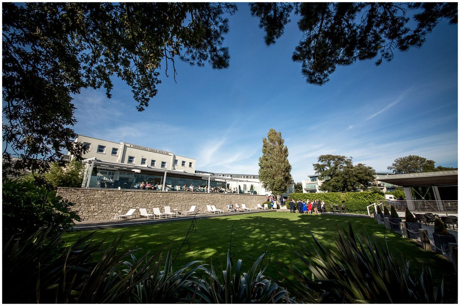 A panoramic sequence showing a school campus with white buildings, green lawns, and trees under a blue sky.