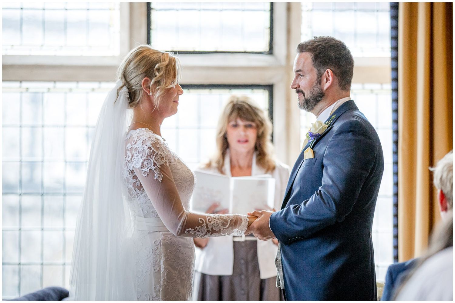 A couple exchanges vows during an indoor wedding ceremony with an officiant standing between them.