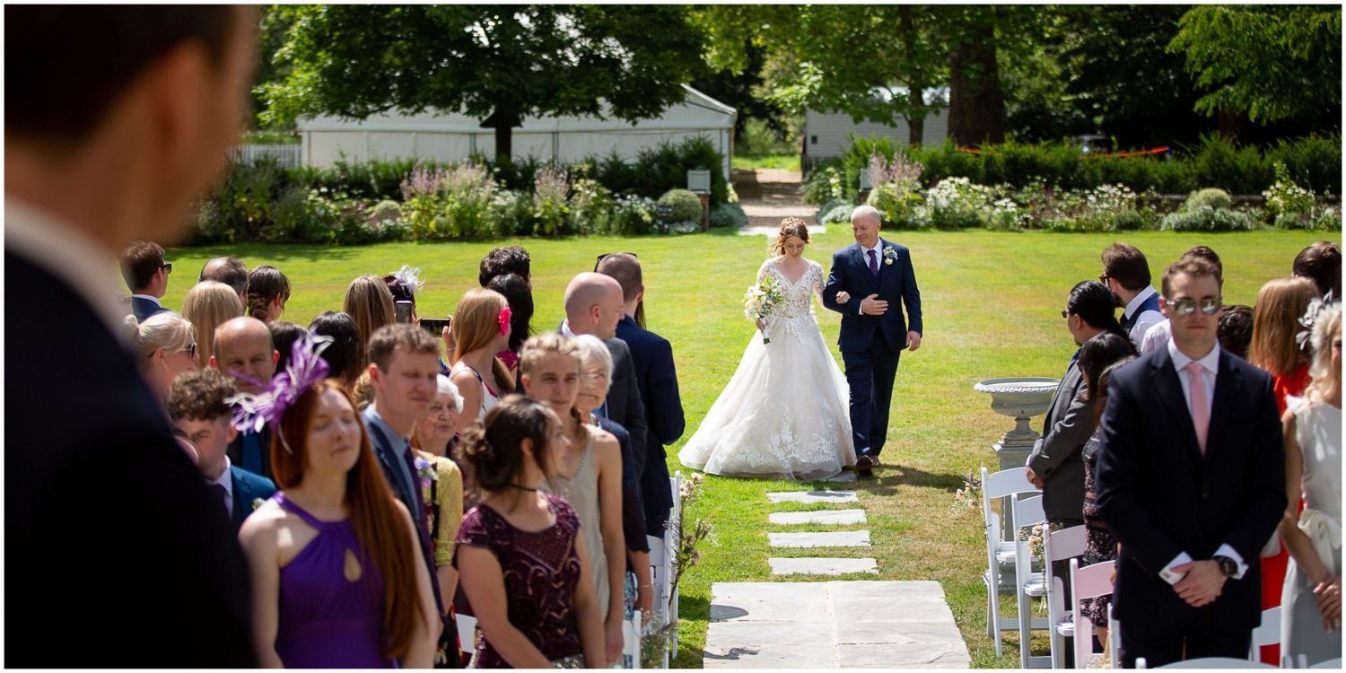 Wedding guests gather outdoors on a sunny day to celebrate at an elegant garden ceremony.