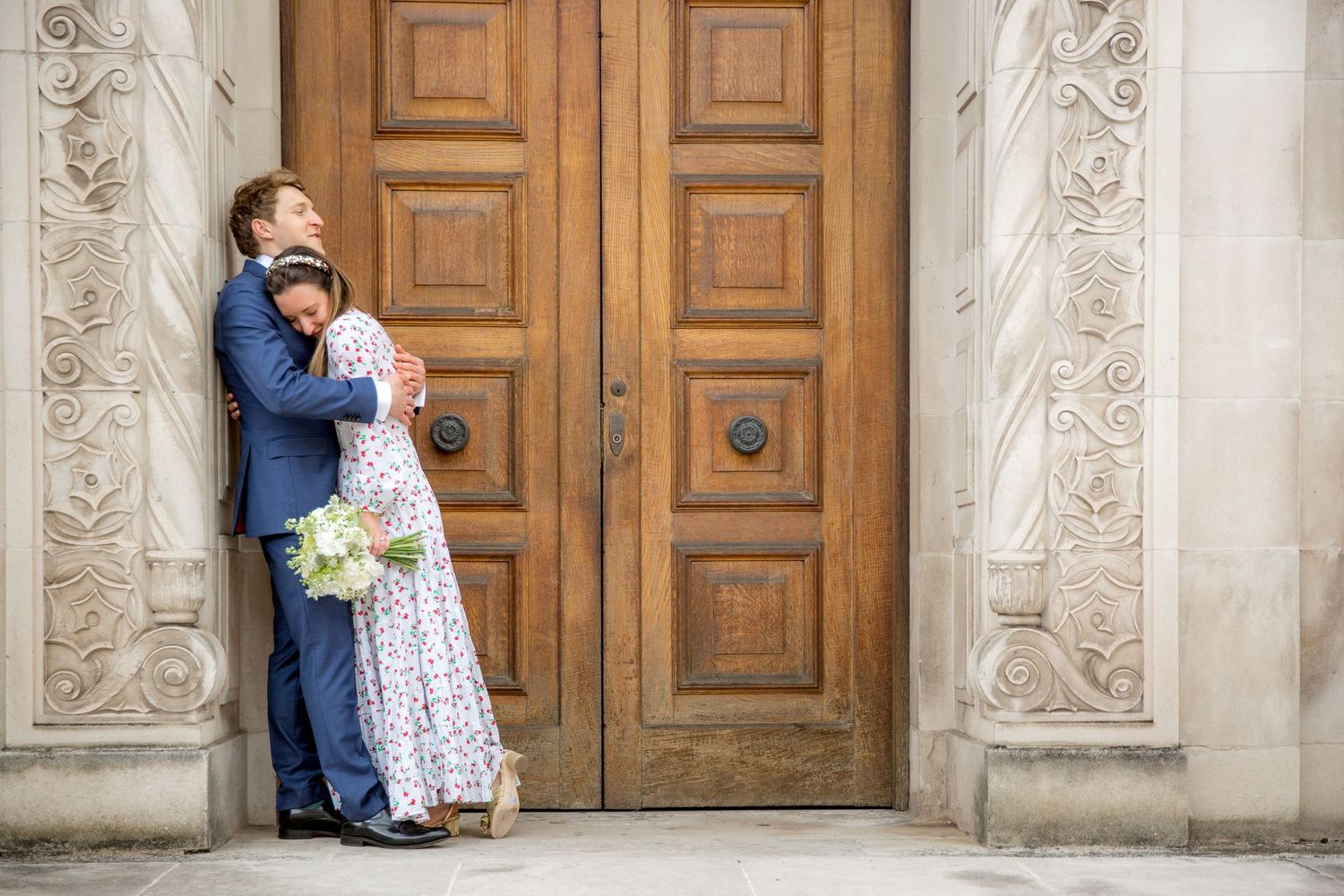 A couple shares a romantic moment in front of ornate wooden doors and stone columns during a wedding photo session.
