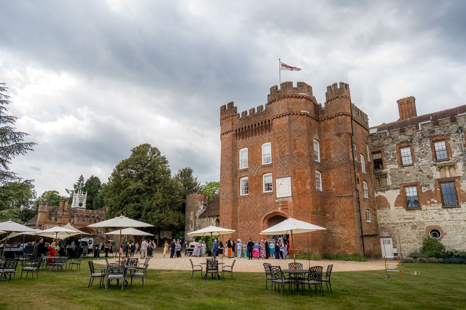 Panoramic view of historic brick castle venue with outdoor seating under cloudy sky.