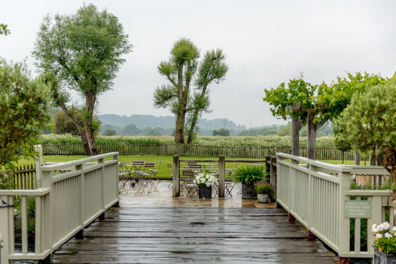 Wooden boardwalk path over flooded waters leading through trees and greenery on a cloudy day.