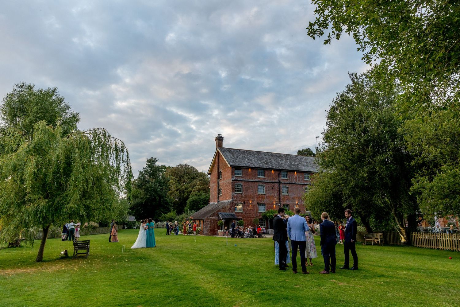 Wide landscape view of a wedding venue grounds with guests gathered under cloudy skies.