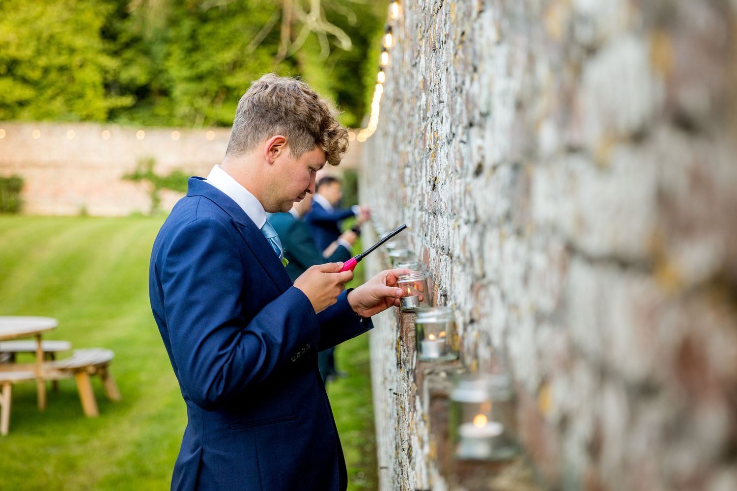 People in formal attire checking phones against rustic brick wall.