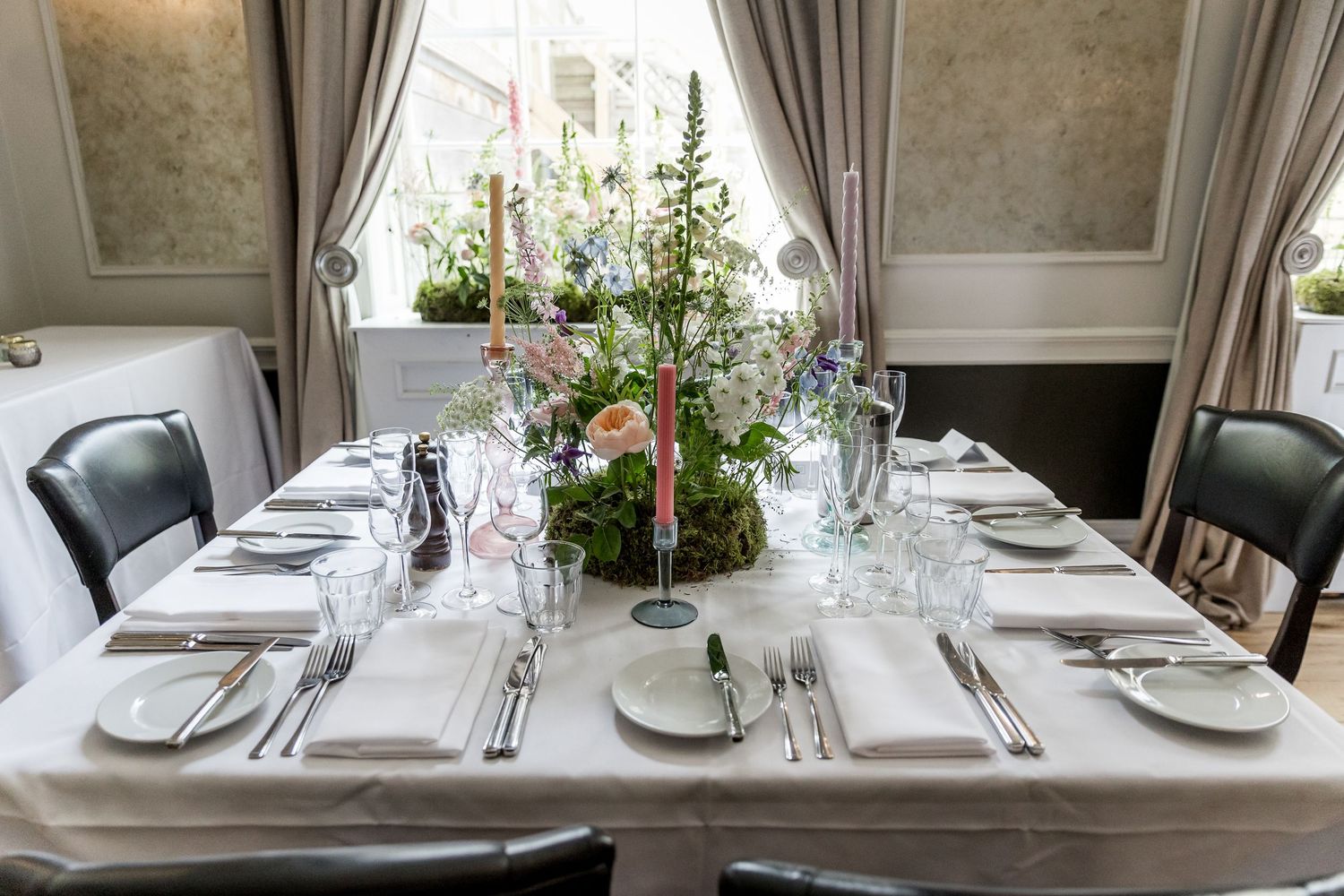 Formal dining table settings with white linens and natural light streaming through curtained windows.
