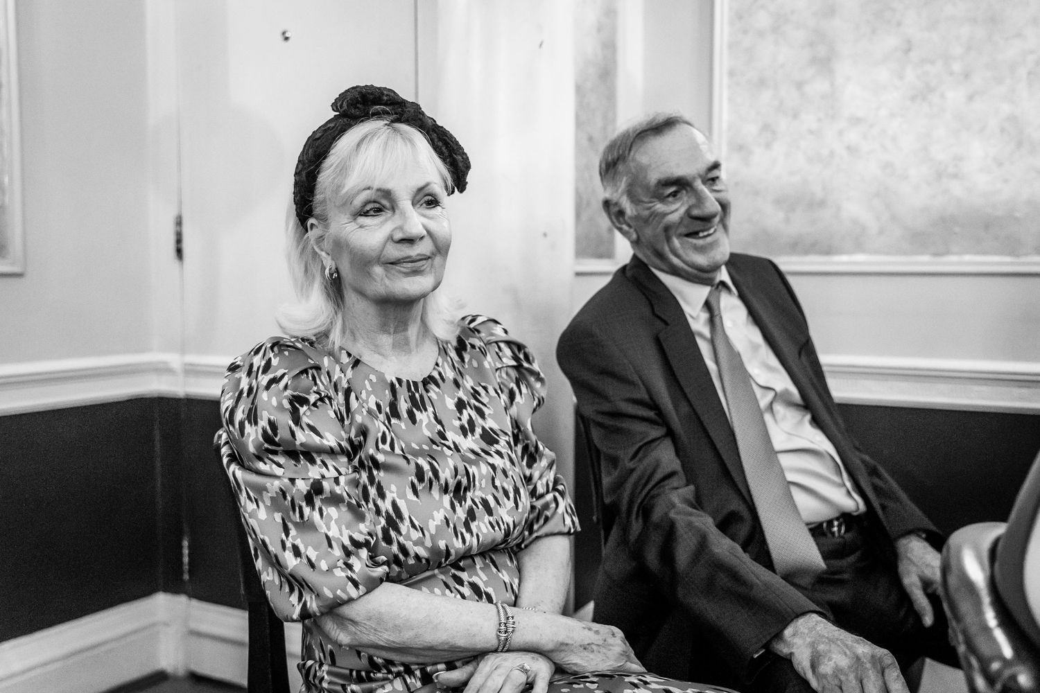 A black and white photo of wedding guests seated and smiling during the ceremony.