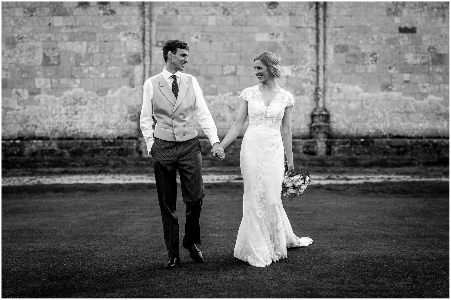 Wedding couple poses for romantic portraits along rustic stone wall in black and white.