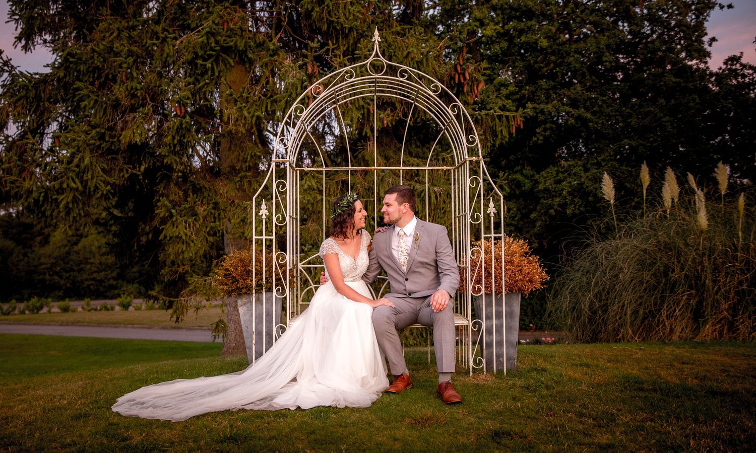 Wedding photograph of the bride and groom sat by the pergola at Southdowns Manor in the Summer evening light