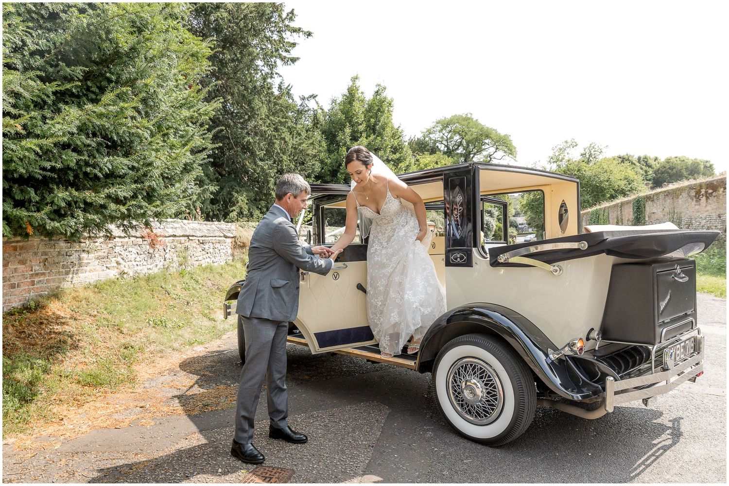 Classic vintage wedding car decorated with ribbons and flowers parked outside a historic building.