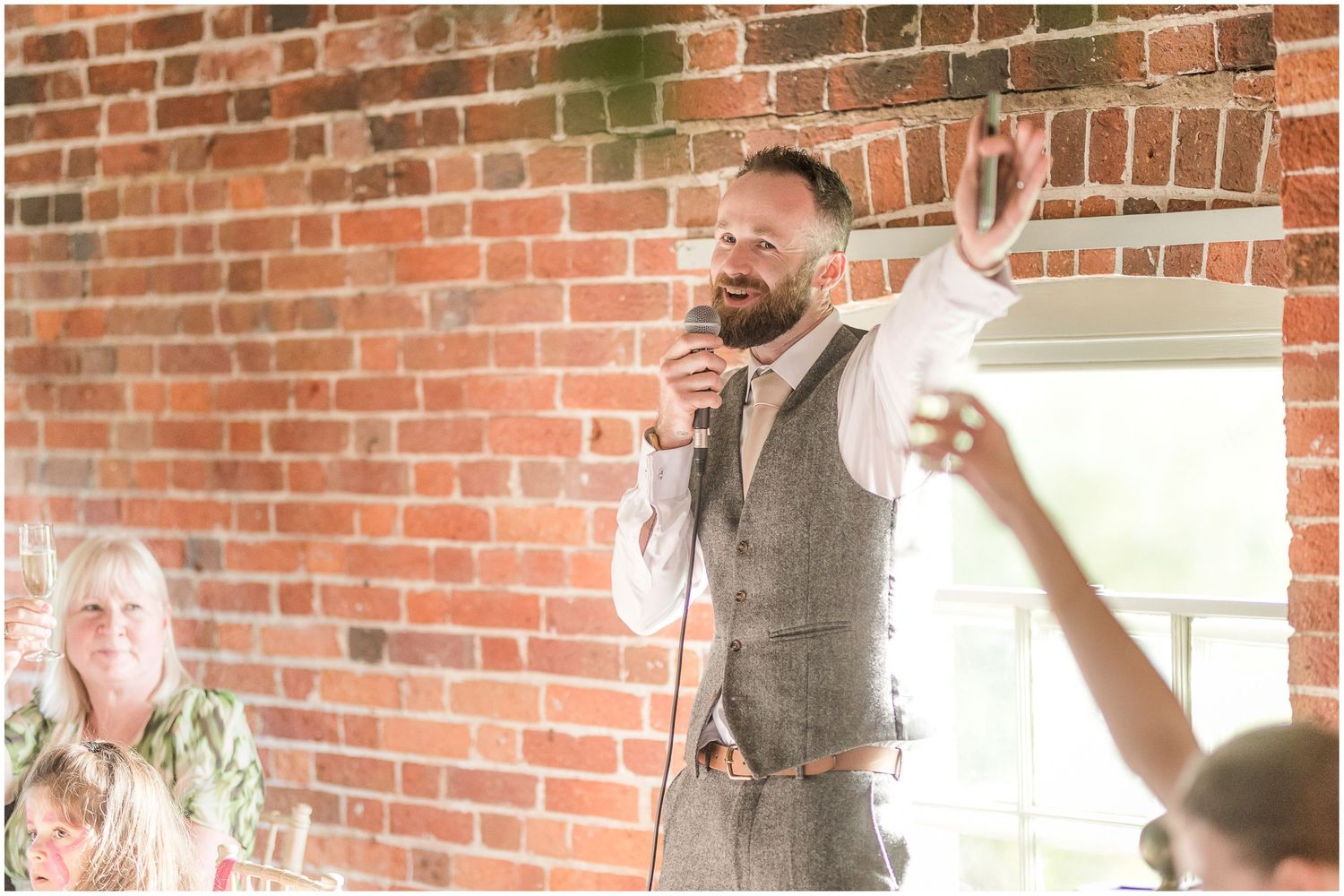 Guests toast and celebrate during wedding reception against exposed brick wall backdrop.