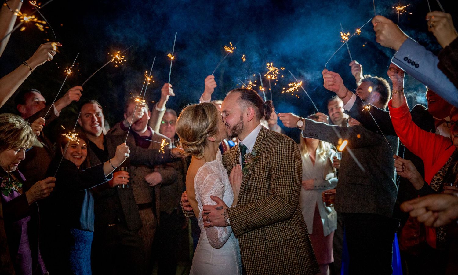 Wedding celebration at night with guests holding sparklers creating light trails.
