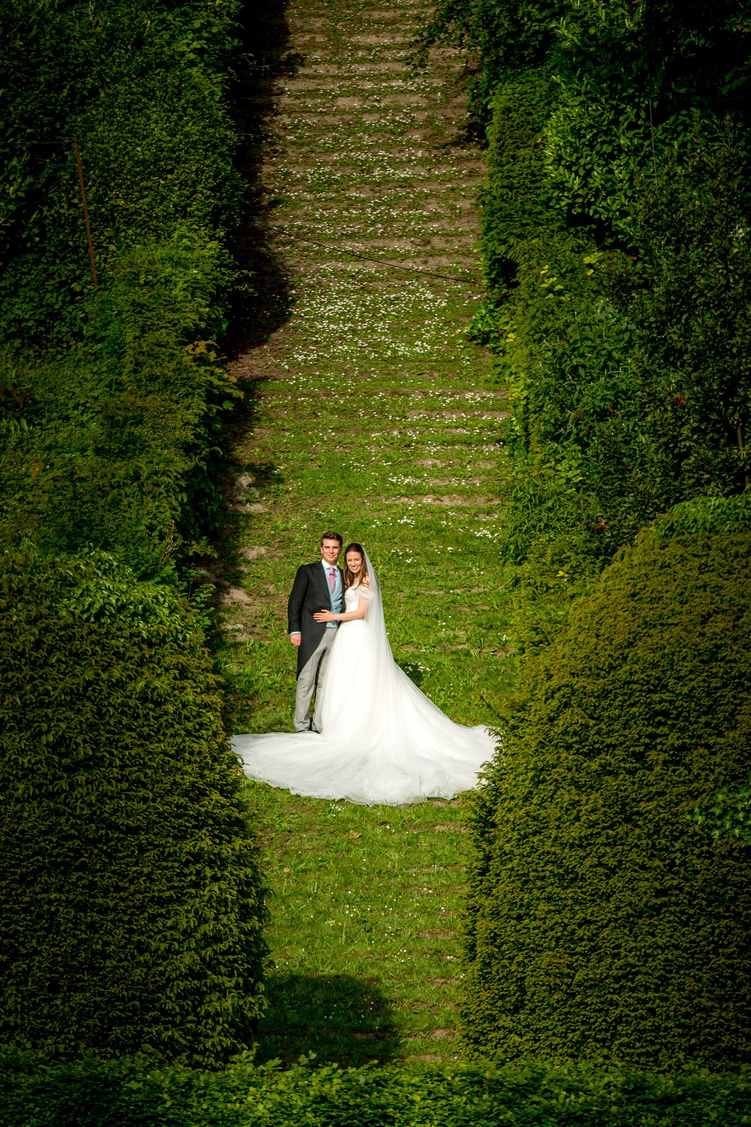 A couple poses for romantic wedding photos on a lush green lawn surrounded by trees.