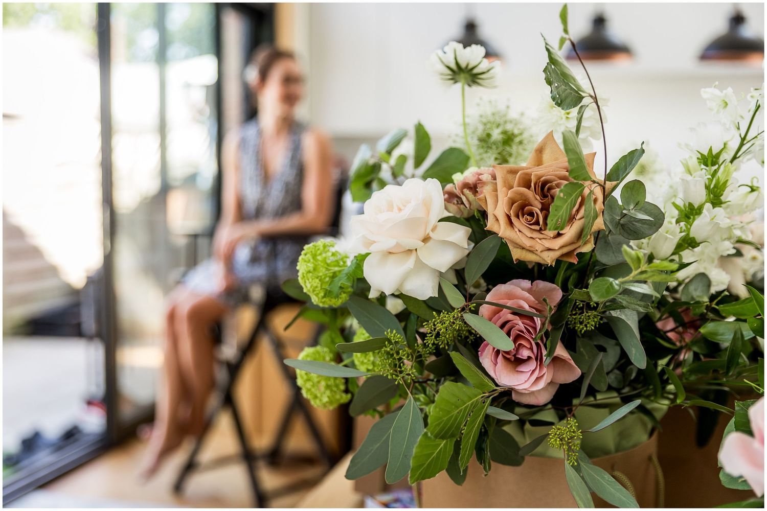 Details of wedding flowers with the bride in the background during pre-ceremony preparations.