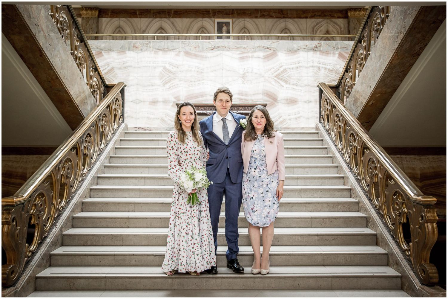 Elegant wedding couple poses on grand marble staircase with ornate railings.