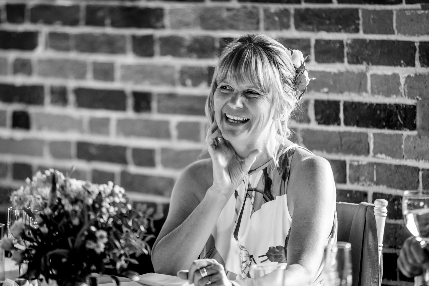 Wedding guests share laughter and conversation during an indoor reception at a rustic brick venue.