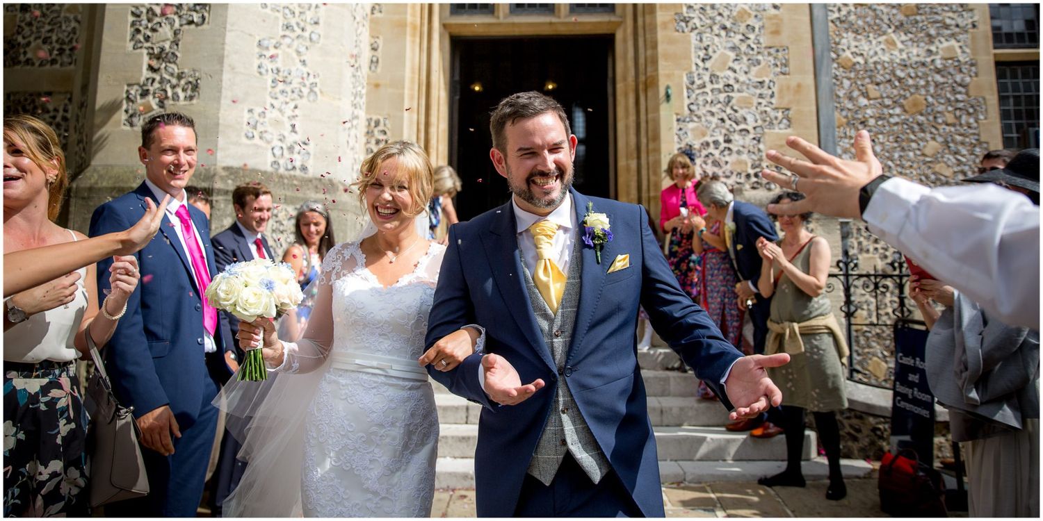 Joyful wedding party exits church while guests toss confetti in celebration of the happy occasion.
