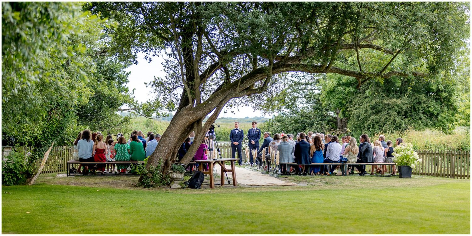 Panoramic view of wedding ceremony location with green landscaping and brick building.