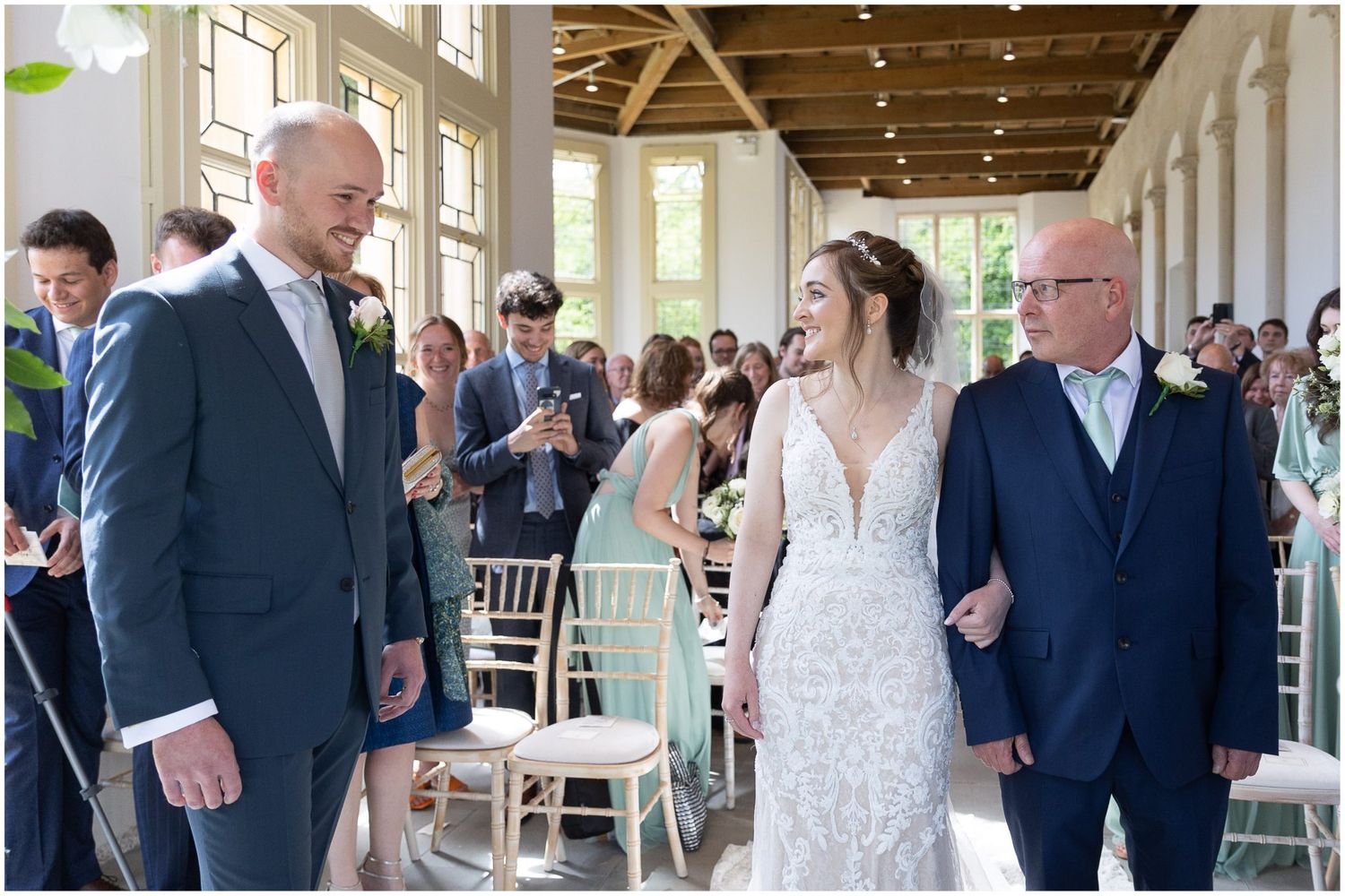 Wedding ceremony in bright venue with white columns and hanging lights.