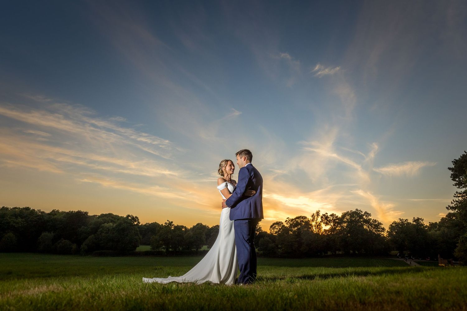 Silhouette of a couple against a dramatic sunset sky in an open field.