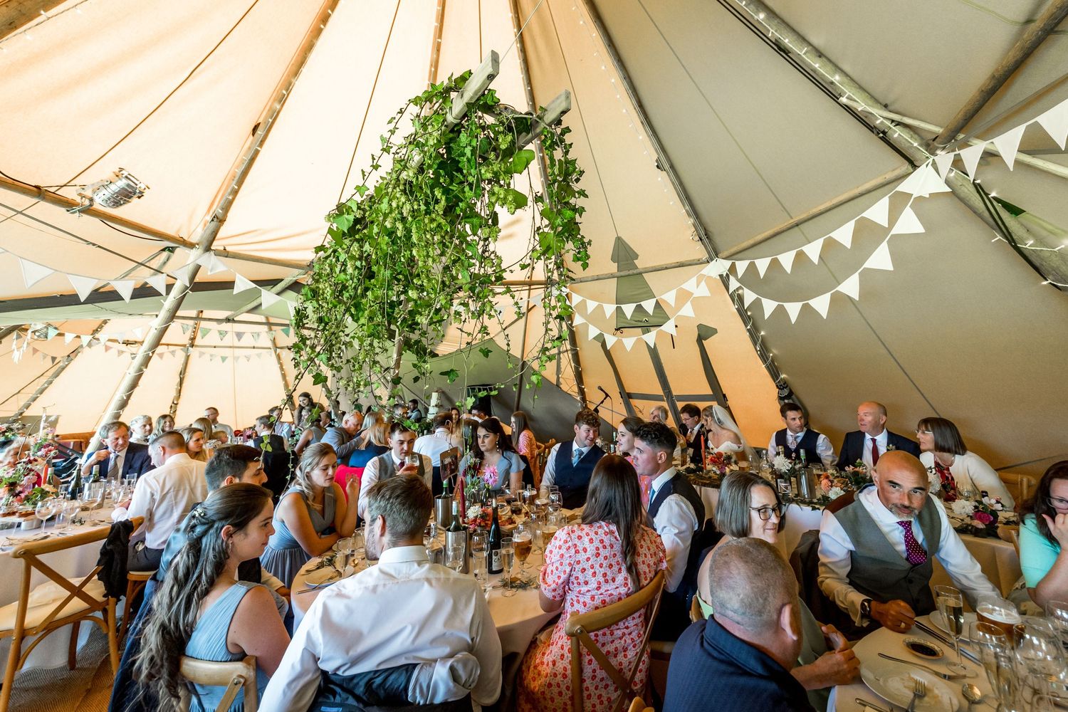 Interior view of a wedding reception in a tipi tent with string lights and greenery decorations.