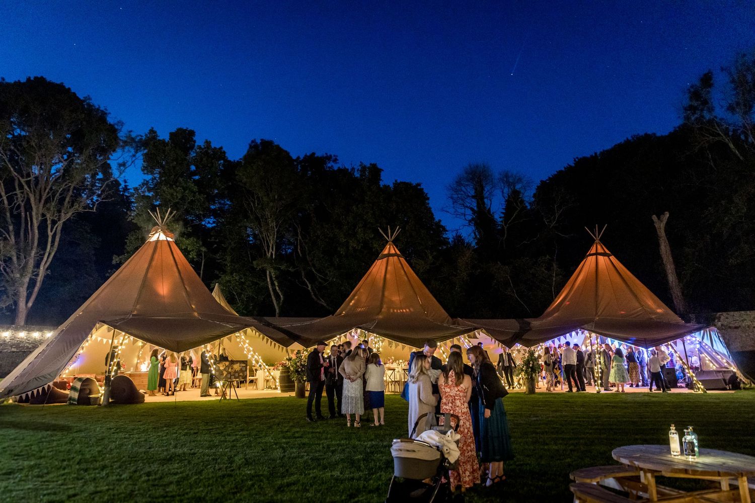Illuminated tipi tents glowing at dusk during an outdoor wedding reception.