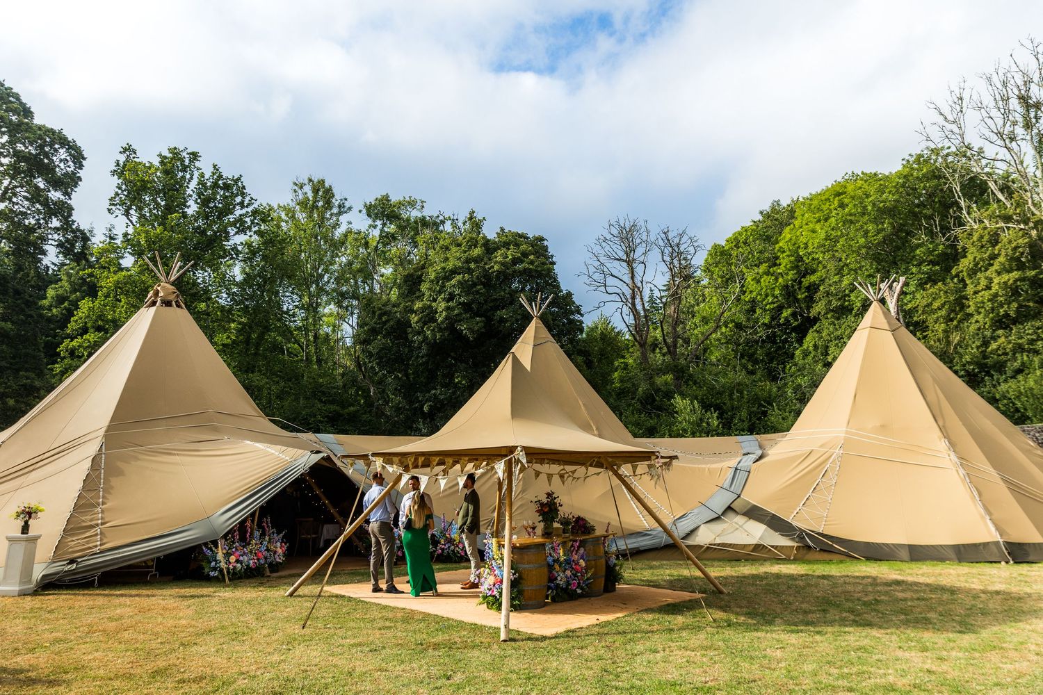 Multiple teepee-style canvas tents arranged in a field under blue skies for an outdoor event.