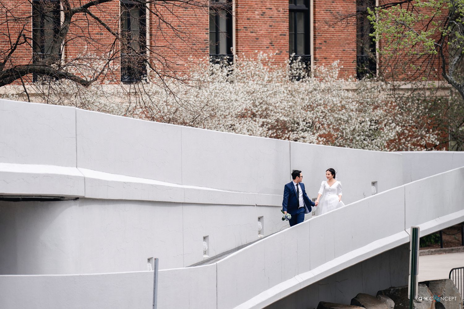 Two people walk together on a curved white concrete ramp against a brick building backdrop.