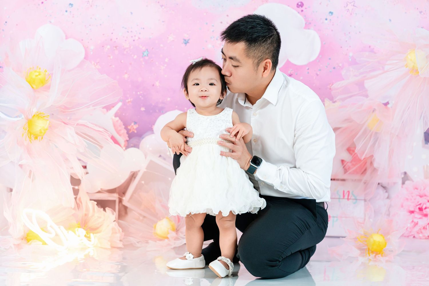 A tender moment captured against a pink floral background with white balloons.
