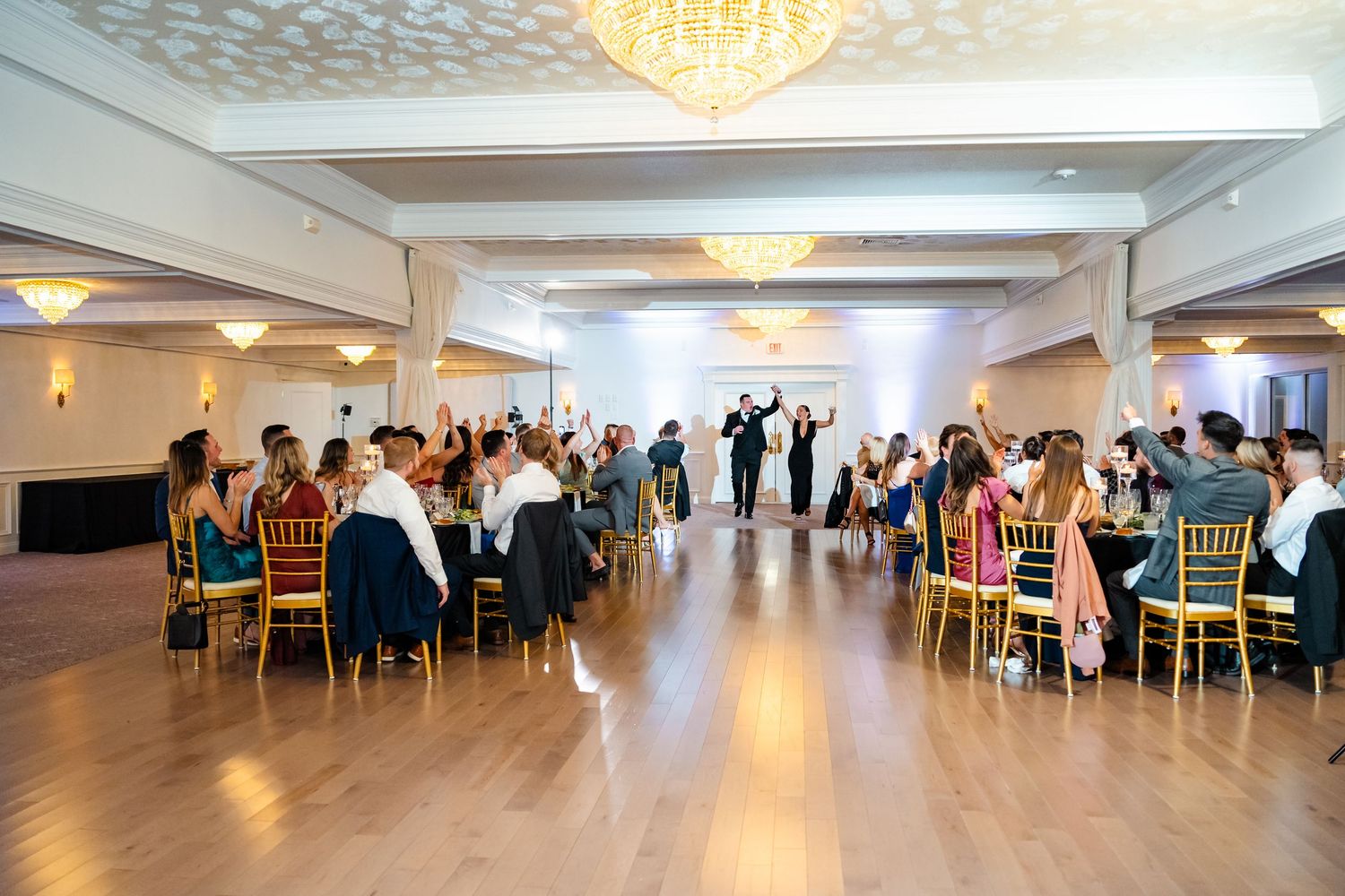 Panoramic view of wedding reception hall with elegant lighting and gold chiavari chairs.