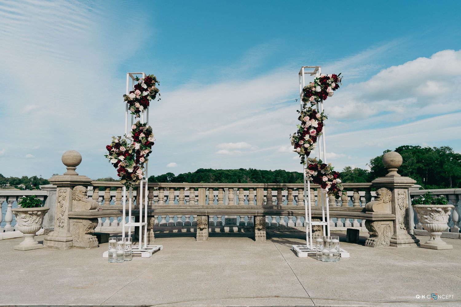 Panoramic view of a classical stone balustrade with ornate columns against a bright blue sky and white clouds.