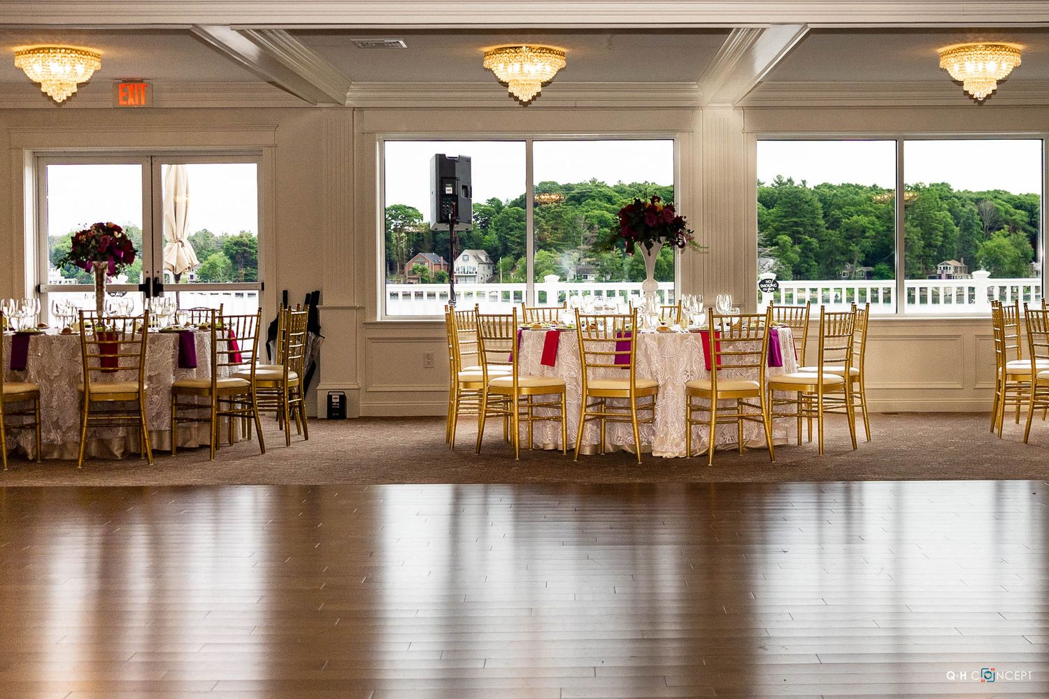 Spacious ballroom with round tables, chiavari chairs, and large windows offering natural light and water views.