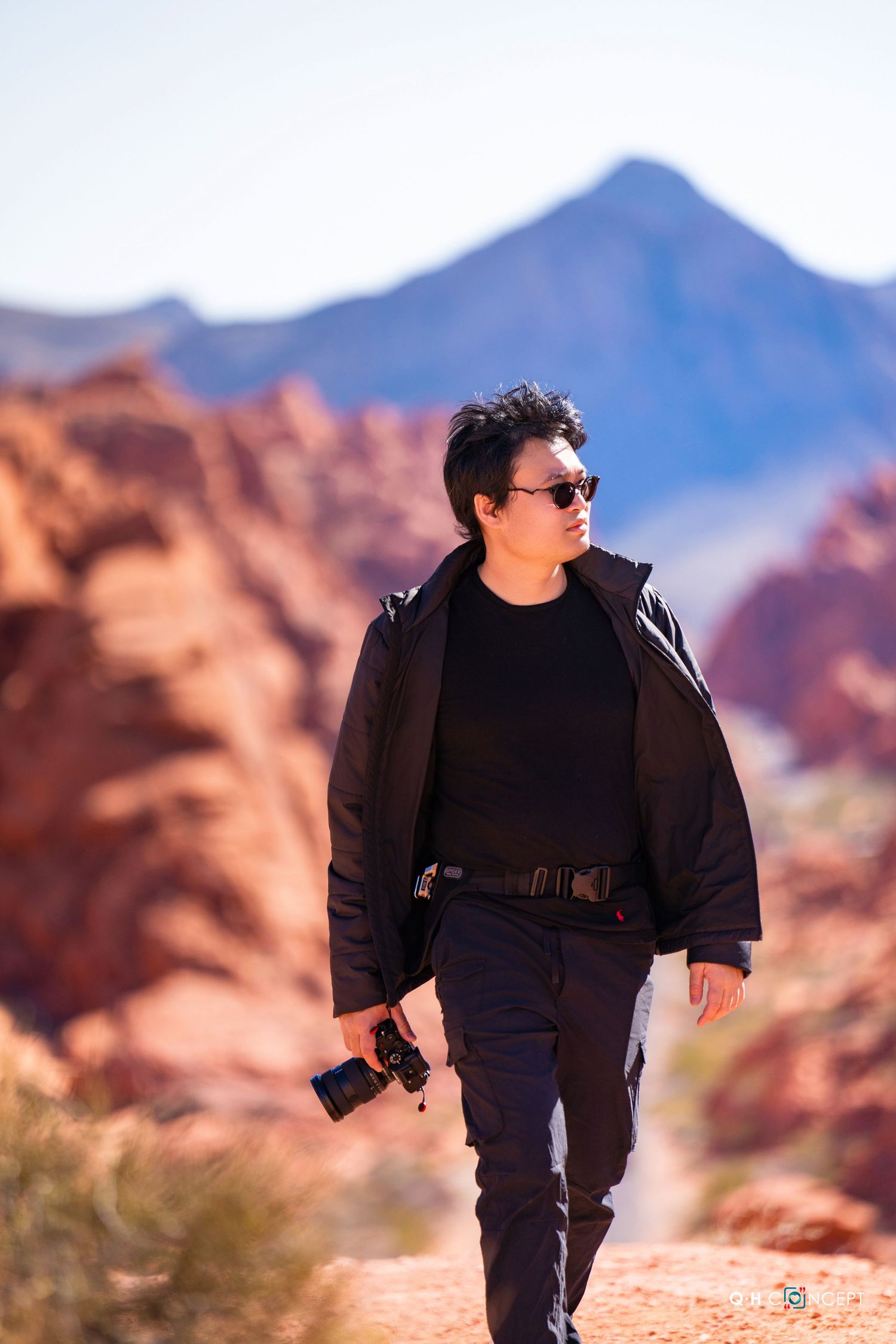Person dressed in black exploring rocky desert terrain with mountains in background.