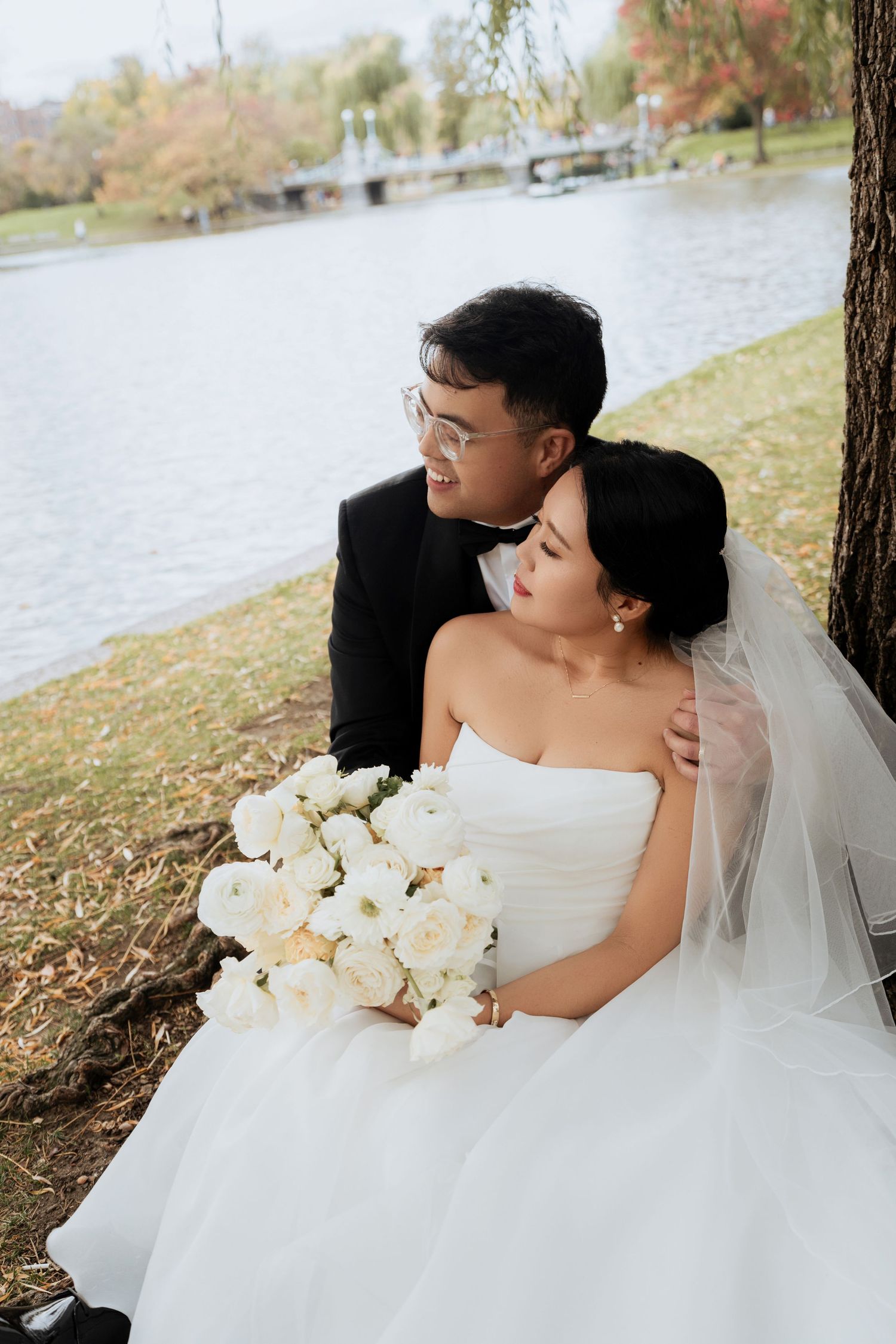 A bride in a white gown holds a bouquet of white flowers in an outdoor autumn setting.