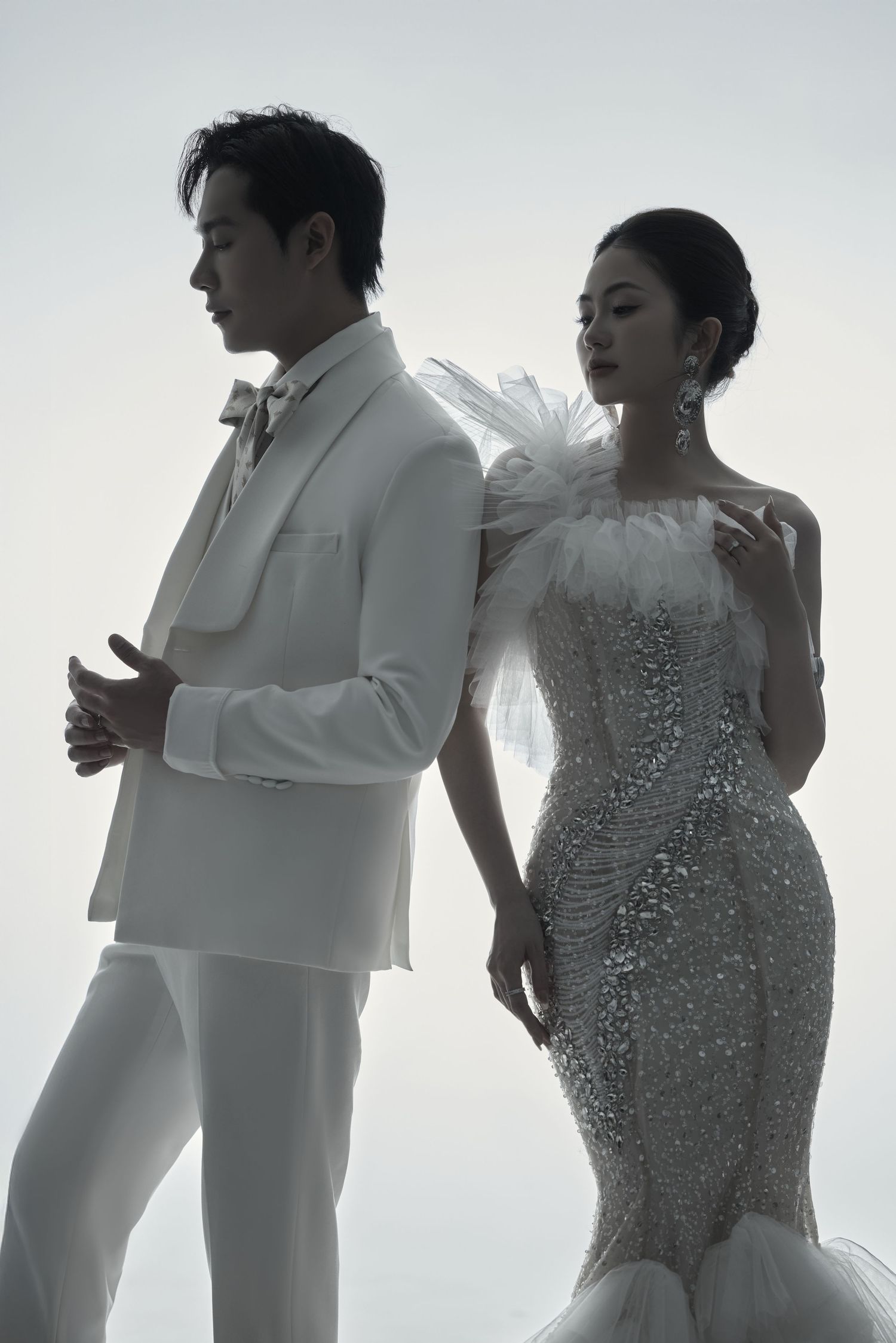 Silhouetted couple in white wedding attire pose against bright background in romantic series of photos.