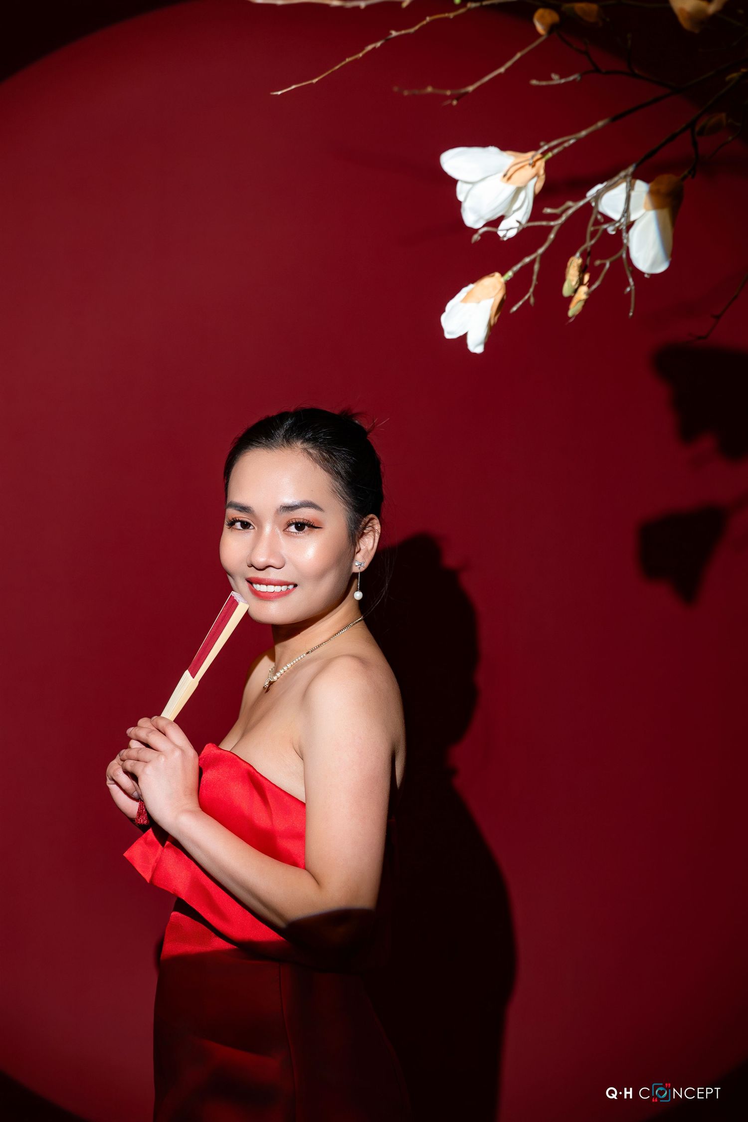 A woman in a red dress poses against a deep burgundy background with white flowers creating an artistic composition.