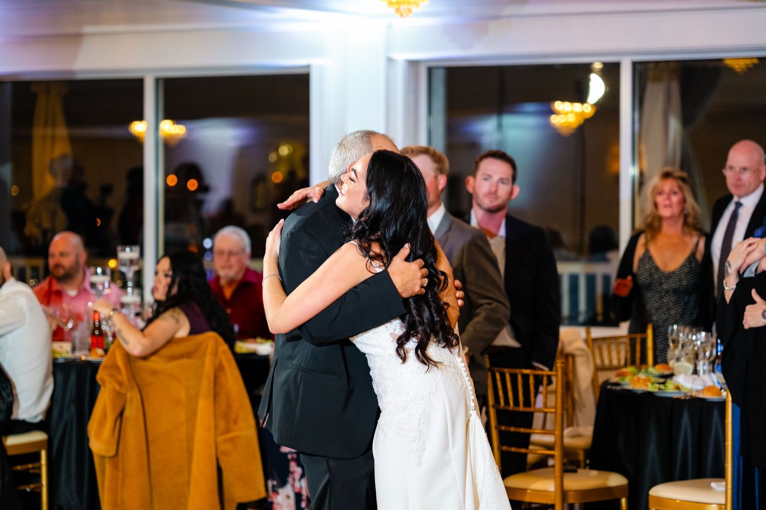 Evening wedding reception with guests mingling and dancing in an elegant ballroom setting.