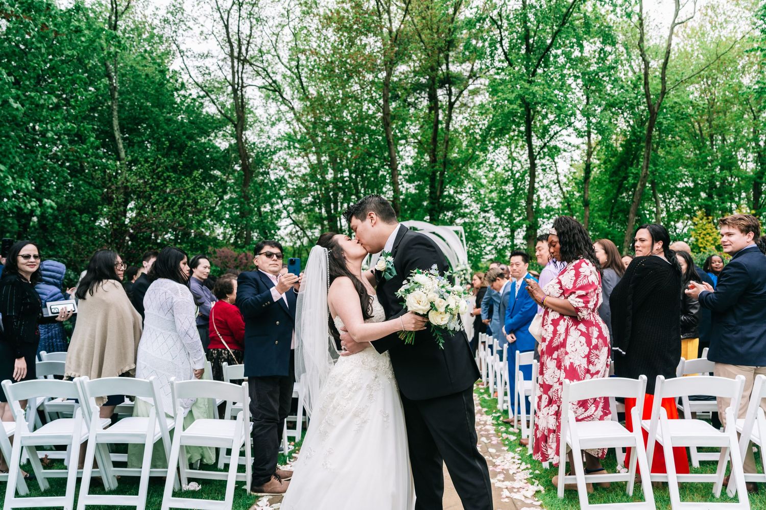 Wedding ceremony in a lush outdoor garden setting with white chairs and floral arrangements.
