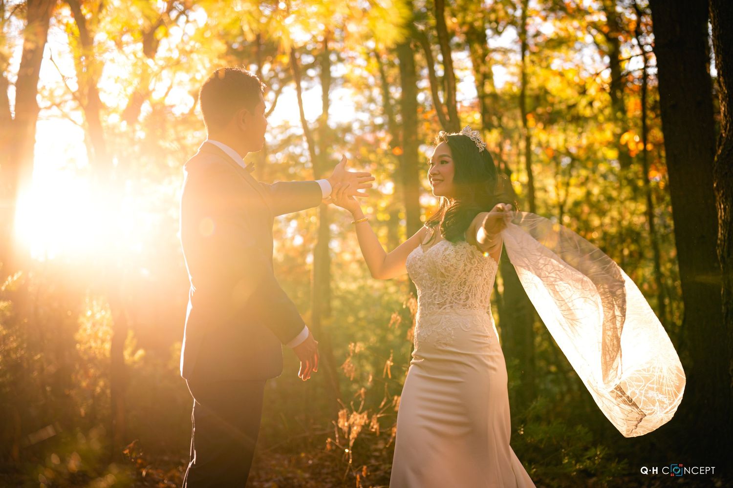 A sunset wedding portrait with golden light streaming through trees as the veil catches the breeze.