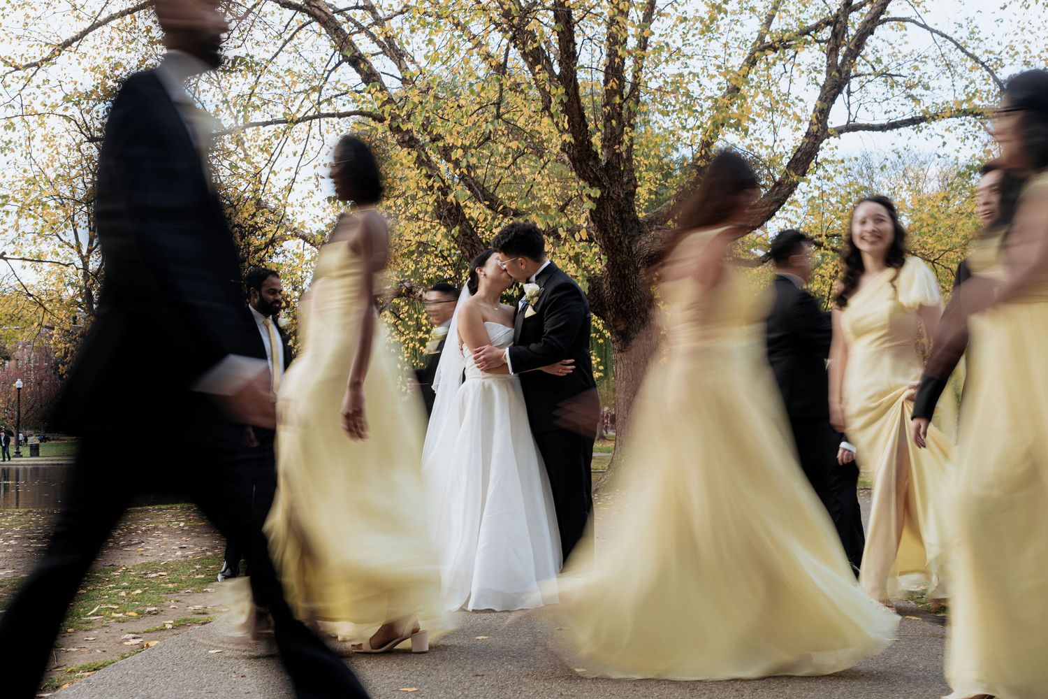 Motion-blurred wedding party walking in pale yellow dresses creating dreamy effect.