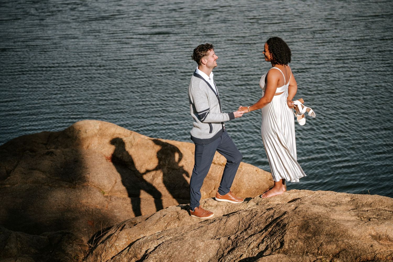 Couple sharing a special moment on coastal rocks during a seaside proposal.