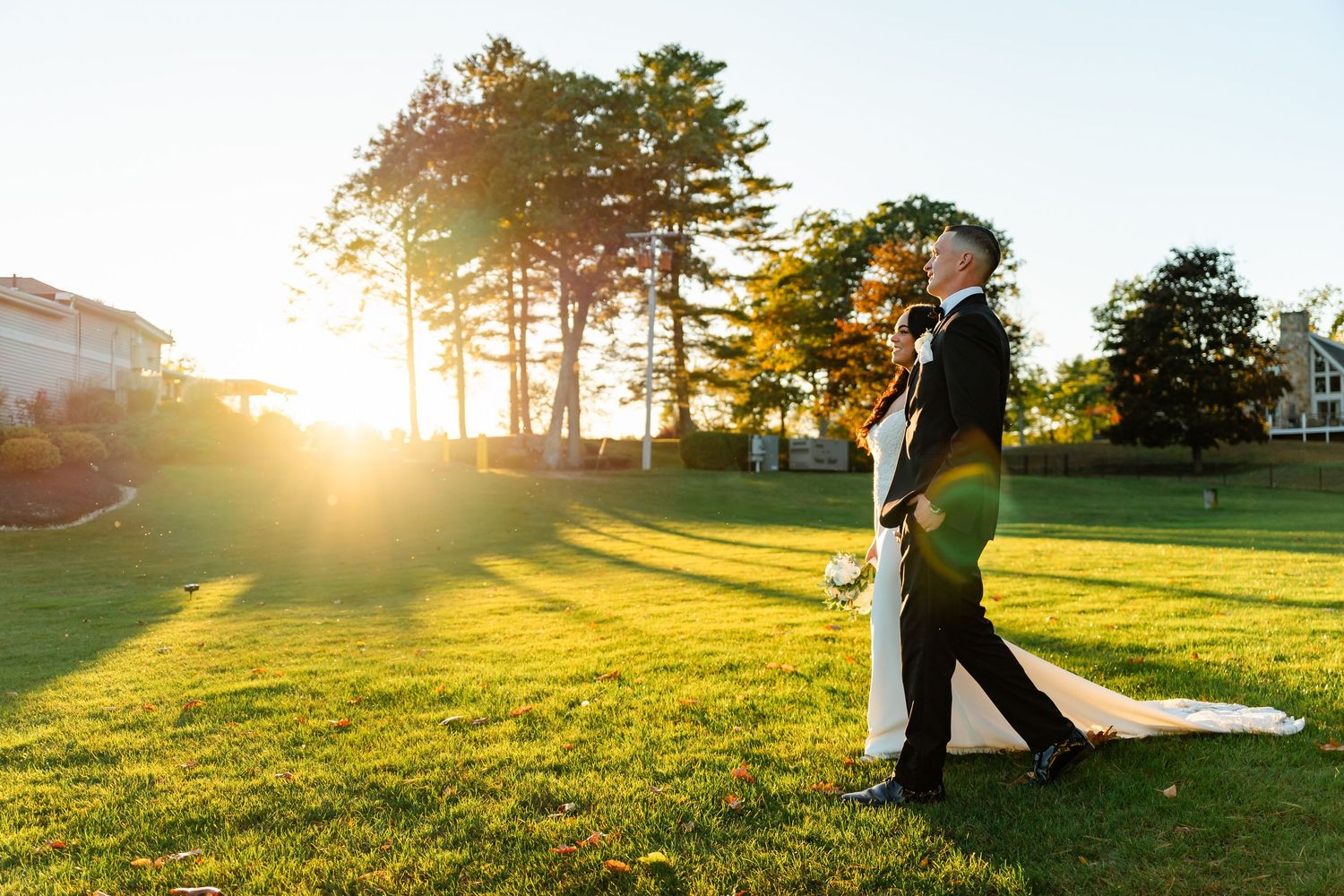 Romantic couple silhouetted against golden sunset in grassy field with trees in background.