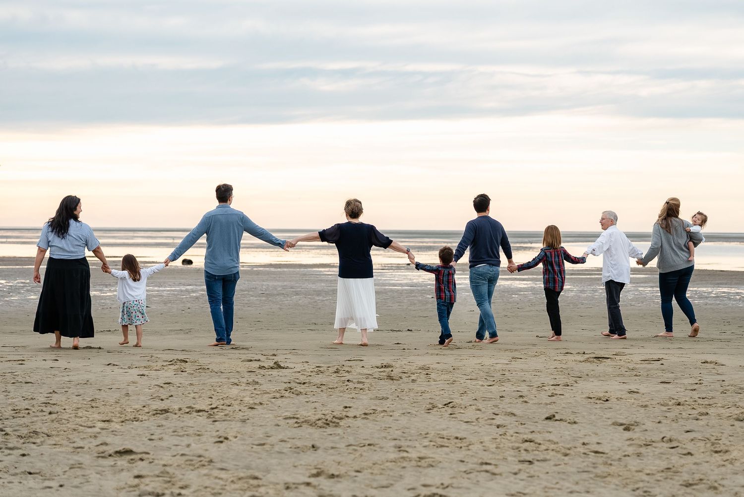 A group of people holding hands while walking in a line along a sandy beach at sunset.